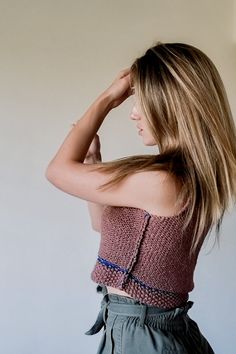 a woman with long hair standing in front of a white wall and looking off to the side