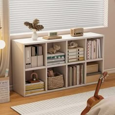 a living room with bookshelves and a guitar on the floor next to a window