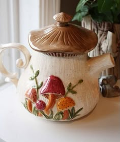 a ceramic teapot with mushrooms and leaves painted on it