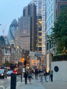 many people are walking on the sidewalk in front of tall buildings and skyscrapers at dusk