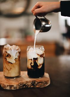 two glasses filled with iced coffee on top of a wooden table next to each other