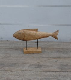 a wooden sculpture of a fish sitting on top of a wooden floor next to a white wall