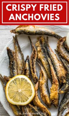 crispy fried anchovies on a white plate with lemon wedges