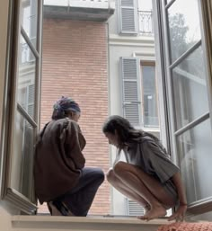 two people sitting on a window sill in front of a brick building