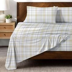 a bed with plaid sheets and pillows on top of it in a bedroom next to a night stand