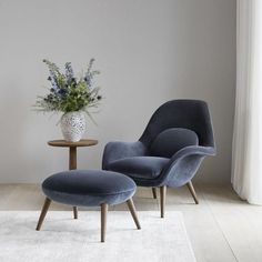 a blue chair and ottoman in front of a white vase with flowers on the table