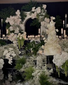 a wedding cake surrounded by white flowers and greenery in front of a black backdrop