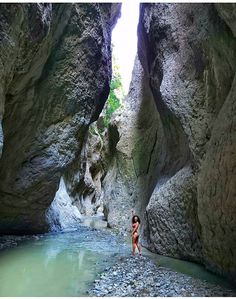 a woman standing in the middle of a river between two large rocks, with water running through them