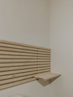 a white toilet sitting next to a wooden shelf in a bathroom under a window with blinds on it