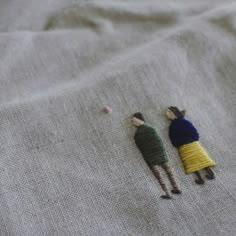 two miniature people standing next to each other on top of a white cloth covered surface