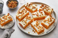 several pieces of carrot cake sitting on a plate next to bowls of nuts and water