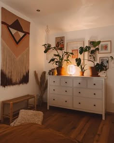 there is a dresser with plants on it in the corner and pictures hanging on the wall