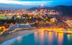 an aerial view of the beach and city lights at night, with mountains in the background