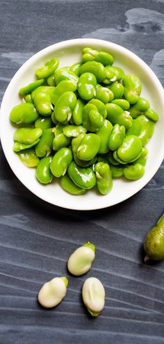 a white bowl filled with green beans next to a pickle on top of a table