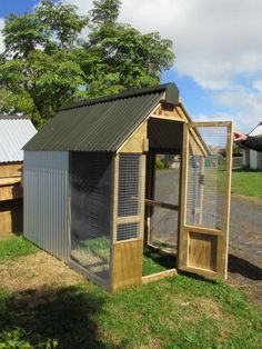 a small chicken coop in the grass next to a building with a door and window