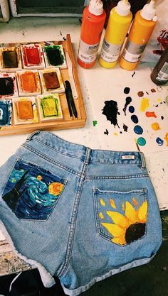 a pair of jean shorts with sunflowers painted on them next to paintbrushes