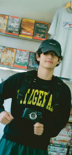 a young man wearing a hat and holding a camera in front of a store display