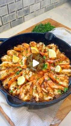 a skillet filled with shrimp and lemons on top of a wooden cutting board