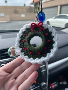 a hand holding a crocheted christmas wreath ornament in front of a car