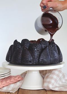 someone pouring chocolate sauce on top of a bundt cake