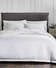 a bed with white sheets and pillows in a small room next to a night stand