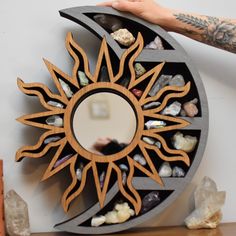 a person holding a mirror with rocks in the middle and a sun design on it