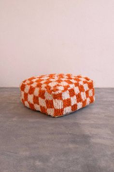 an orange and white checkered ottoman sitting on top of a cement floor next to a wall