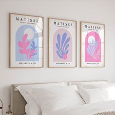 three posters on the wall above a bed in a room with white sheets and pillows