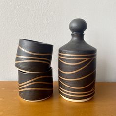 two black vases sitting on top of a wooden table next to each other,