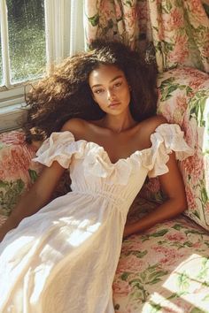 a woman in a white dress sitting on a floral couch with her hair blowing in the wind