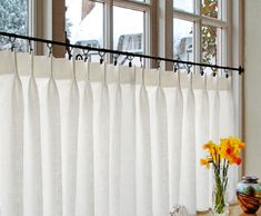 a vase with yellow flowers sitting in front of a window next to a white curtain