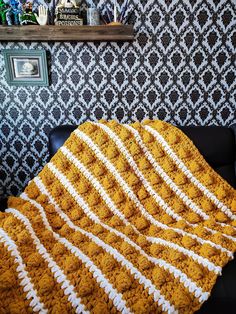 a yellow and white crocheted blanket sitting on top of a black leather couch