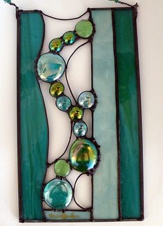 a stained glass panel with green and blue designs on the bottom, hanging from a white wall