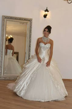 a woman standing in front of a mirror wearing a wedding dress with beading on it