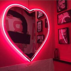 a heart shaped neon sign in the corner of a room with pictures on the wall