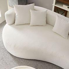 a white round couch with four pillows on it