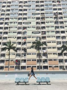 a person sitting on a bench in front of a tall building with balconies