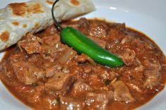 a white plate topped with meat and a green pepper next to a pita bread