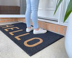 a woman is standing on the door mat that says welcome to our home and there is also a potted plant