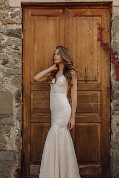 a woman standing in front of a wooden door wearing a wedding dress with an open back