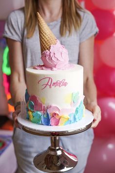 a woman holding a birthday cake with an ice cream cone on top and pink frosting