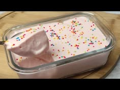 a container filled with white frosting and sprinkles on top of a wooden cutting board