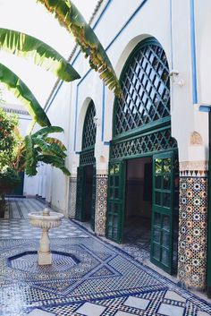 an ornate courtyard with tiled floors and green doors, surrounded by palm trees in the background