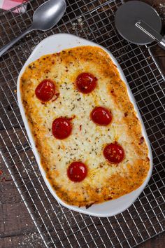 a square pizza with pepperoni and cheese on a cooling rack next to utensils