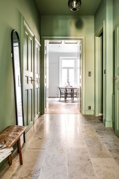 an empty hallway with green walls and white tile on the floor next to a wooden bench