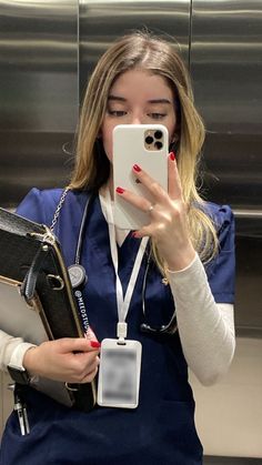 a woman in scrubs taking a selfie with her cell phone while holding a folder