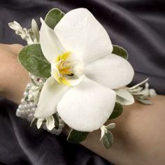 a woman's arm with a white flower and green leaves on it, along with pearls