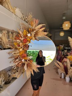 a woman standing in front of a mirror with dried flowers