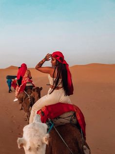 two women riding camels in the desert with one woman covering her eyes and another person wearing