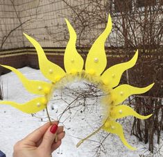 a person holding up a fake sunflower with pearls on it's head in the snow